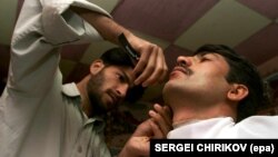 Этот снимок сделан в 2001 году, когда в Афганистан вошли войска США, после чего пал режим талибов, запрещавший брить бороды. Парикмахер бреет клиента, который решил избавиться от бороды. Талокан, 20 ноября 2001 года.