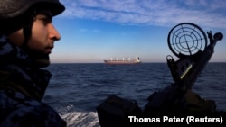 A Ukrainian coast guardsman mans a gun on a patrol boat as a cargo ship passes by in the Black Sea in February 2024. 