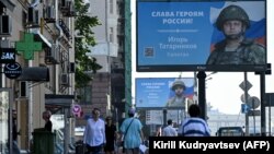 Oamenii trec pe lângă panouri publicitare care prezintă soldați ruși, cu sloganul „Glorie eroilor Rusiei”, pe o stradă din Moscova, august 2022.