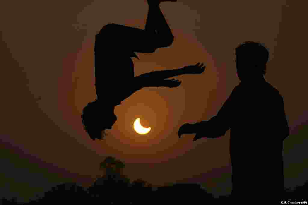 Eclipsa parțială de soare. Niște tineri sar pe o trambulină la periferia orașului Lahore, Pakistan, pe 25 octombrie.