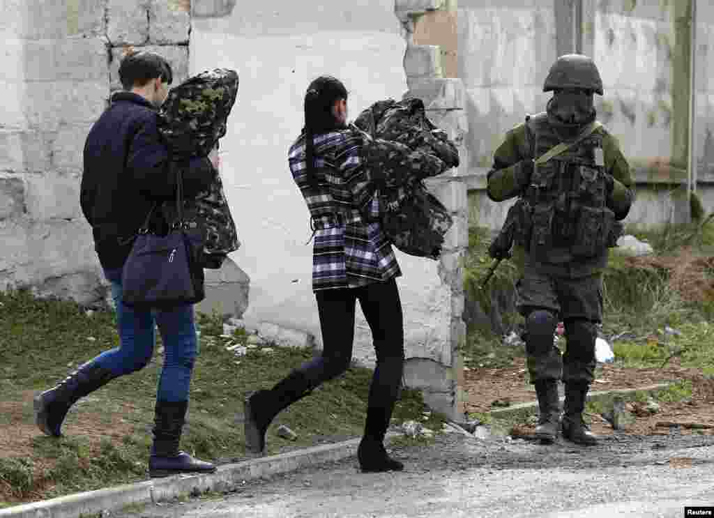 Українські жінки-вояки йдуть зі служби повз озброєного російського військового поруч із частиною А2320 у смт Перевальне, під Сімферополем, 19 березня 2014 року