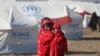 An Afghan internally displaced person holds a child and walks near temporary shelters built by the United Nations High Commissioner for Refugees in Herat in December 2018.
