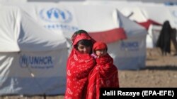 An Afghan internally displaced person holds a child and walks near temporary shelters built by the United Nations High Commissioner for Refugees in Herat in December 2018.
