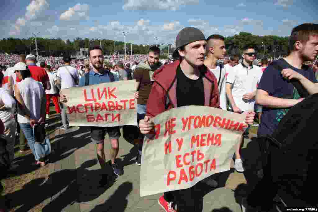 Молодий чоловік (праворуч) тримає у руках плакат:&nbsp;&laquo;Я не злочинець, у мене є робота&raquo;. Цей плакат &ndash; посилання на промову Олександра Лукашенка 12 серпня під час чергового засідання президента з правоохоронцями та представниками інших державних структур.&nbsp;&laquo;Основа всіх цих так званих протестувальників &ndash; люди із кримінальним минулим, сьогоднішні безробітні. Немає роботи, значить, &laquo;гуляй дядько по вулицях і проспектах&raquo;. Тому я по-доброму прошу і попереджаю всіх: влаштуватися на роботу тим, хто не працює&raquo;, &ndash; заявив тоді Лукашенко