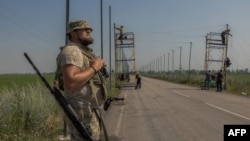 Украинский военный стоит на страже, пока его сослуживцы устанавливают антидроновые сетки над дорогой на востоке Донецкой области, 8 июля 2025 года