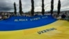 Демонстранты держат гигантский украинский флаг на митинге в поддержку Украины вдоль шоссе Сьюард в Анкоридже, штат Аляска, 14 августа 2025 года, накануне запланированной встречи президентов США и России