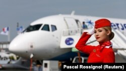 Az Aeroflot orosz légitársaság egyik utaskísérője pózol egy Szuhoj Superjet 100-as repülőgép előtt
